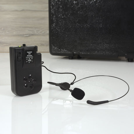 QTX BHS-175.0 VHF headset microphone with black beltpack transmitter and 3.5mm jack lead, shown beside a portable PA speaker on a light surface.