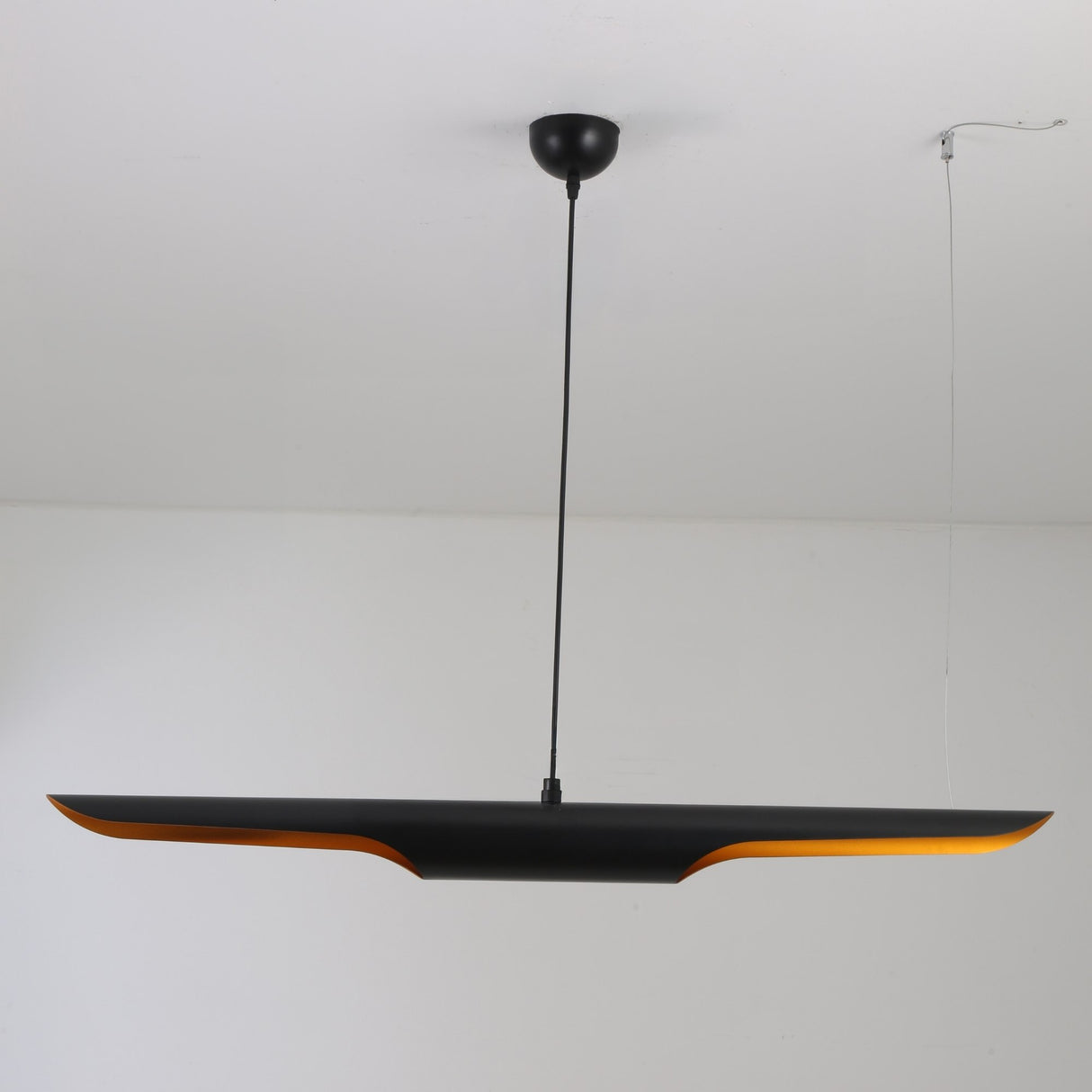 The Stealth 2 Light Linear Suspension in Brass & Black features a sleek modern design with a black horizontal shade and subtle orange glow, suspended from a black cord against a white ceiling for minimalist elegance.