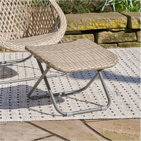 Tobs Outdoor Grey Synthetic Rattan Folding Footstool, 37cm, with woven top and folding steel frame, shown on a patio beside a matching rattan chair.