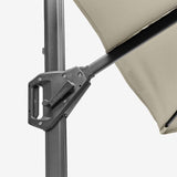Close-up of the Voyager T1 X cantilever parasol's tilt mechanism and hinge joint in dark grey metal, with champagne canopy fabric visible above against a plain background.