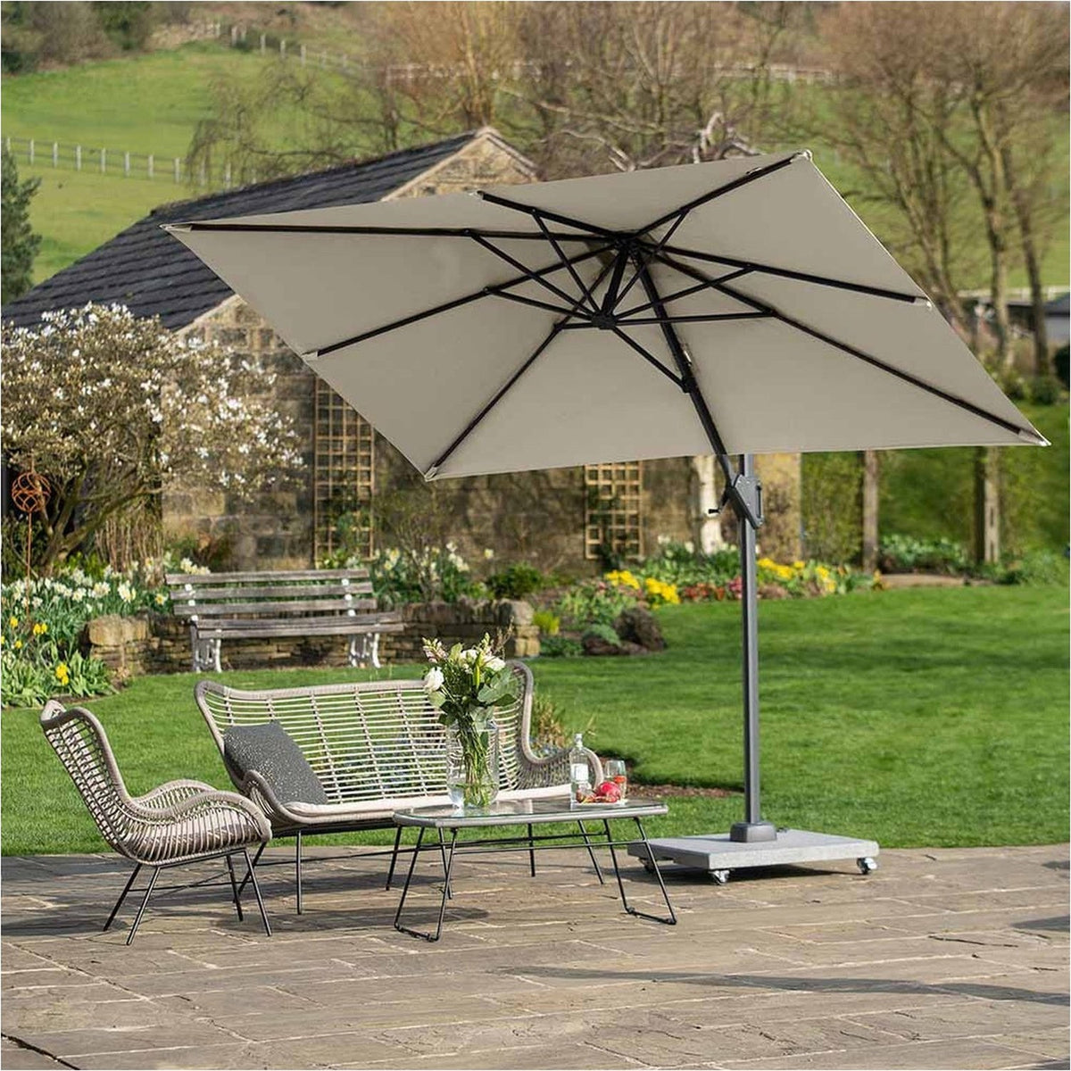 Voyager T1 X rectangular cantilever parasol in champagne with black side arm and weighted stone base, shading a rattan seating set and table on a garden patio.