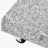 Close-up of the Salerno Hammered Grey 40kg Wheeled Parasol Base corner, showing speckled grey stone texture and a small black castor wheel on white background.
