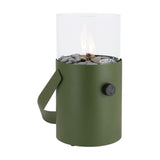 Cosi Moss Green Gas Flame Lantern, 30cm, cylindrical steel body with glass hurricane shade, grey pebbles, gas control knob, and carry handle on a plain white background.