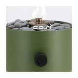 Close-up of the Cosi Moss Green Gas Flame Lantern showing grey pebbles, a brass burner with flame, a green steel body, and a black control knob.
