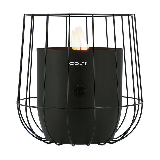 Cosi Basket Black Gas Flame Lantern, 31cm, a cage-style steel fire lantern with lit flame visible inside a black cylindrical burner, control knob on front, plain white background.