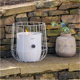 Cosi Basket White Gas Flame Lantern, 31cm, with wire cage frame and lit flame, shown on stone steps beside a decorative vase, outdoor garden setting.