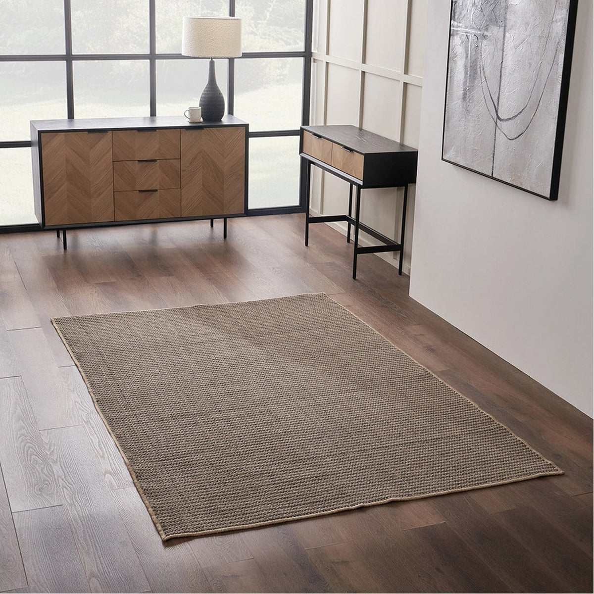 Rectangular natural and slate grey woven rug with a subtle textured pattern, shown on a dark wood floor in a hallway with wooden furniture.
