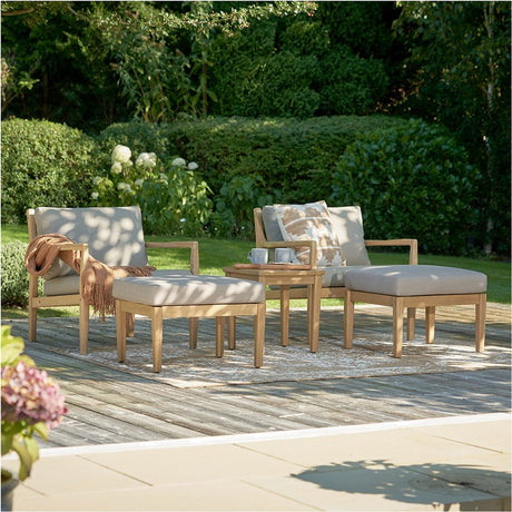 Wooden outdoor lounge set with two armchairs, matching footstools, and a small side table, in light teak-look acacia wood with beige cushions, set on a garden deck.