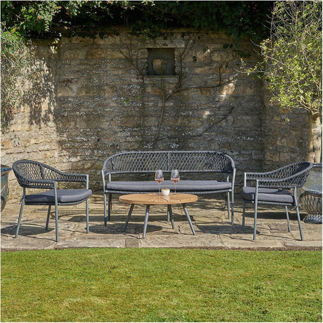 Bazel Outdoor Seating Set featuring a two-seat sofa and two armchairs in black woven wicker with grey cushions, paired with a round wooden coffee table on a stone patio.
