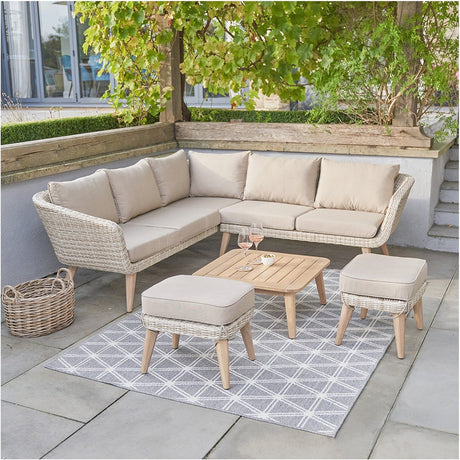 Cabon Outdoor Corner Seating Set with rattan-effect frame, beige cushions, and matching wooden coffee table plus two stools, styled on a patio with a grey patterned rug.