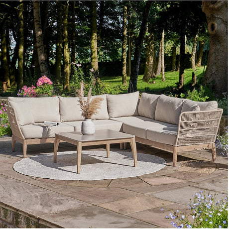 Moeven Outdoor Corner Seating Set with wicker-effect frame and beige cushions, paired with a wood-framed coffee table on a garden patio surrounded by trees and flowers.