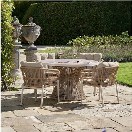 Martic Outdoor 4 Seater Dining Set with round glass-top table and woven aluminium-framed chairs in beige, set on a patio with beige cushions and a garden backdrop.