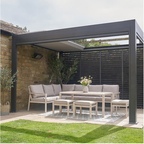 Aruba Outdoor Corner Seating Set in beige, aluminium-framed corner sofa with cushions, matching table and stools under a black pergola on a patio.