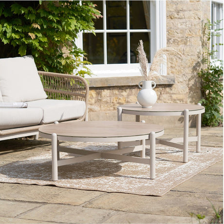 Martic Outdoor Set of 2 Tables, round side tables with beige aluminium frames and wood-effect tops, styled on a patio beside a sofa and stoneware vase.