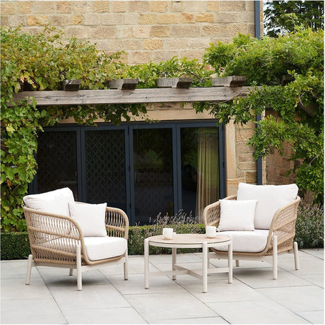 Martic Outdoor Bistro Set with two woven cream armchairs and a round 46cm coffee table, aluminium frames, set on a stone patio against a stone building with climbing greenery.
