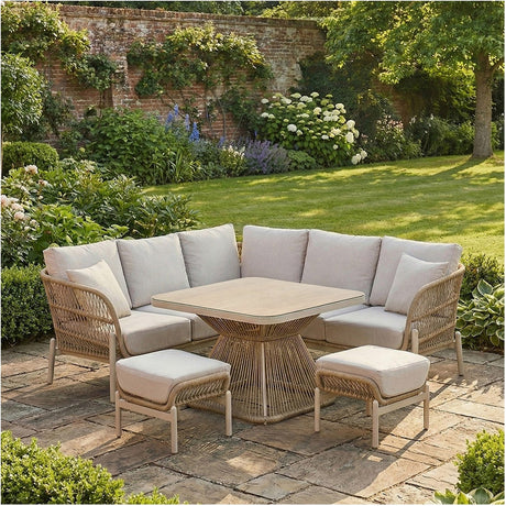Martic Outdoor Corner Seating Set with beige cushions and woven aluminium frame, paired with a square glass-top table and two matching footstools on a garden patio.
