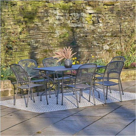 Carlo Rectangular 6 Seater Dining Set in grey mesh steel, with a rectangular table and six matching armchairs on a patio rug against a stone wall garden setting.