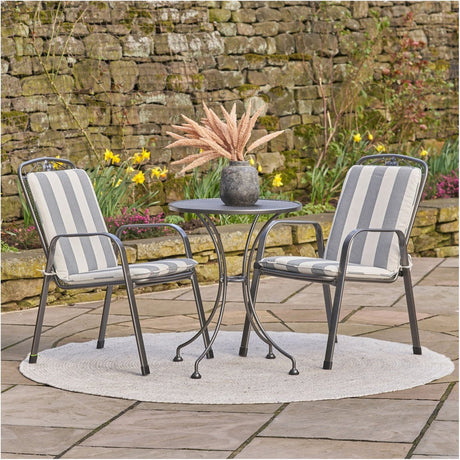 Savoy Bistro Set with Cushions - 92cm: round steel table with two stacking chairs in grey, grey-and-white striped cushions, shown on a patio with stone wall backdrop.