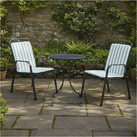 Savoy Bistro Set with two black metal chairs featuring sage green and white striped cushions, paired with a round mesh table, shown on a patio against a stone wall.