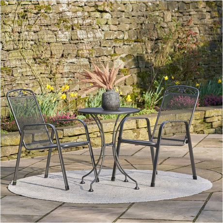 Savoy Bistro Set in iron grey mesh steel, featuring a round table and two mesh-back chairs on a garden patio against a stone wall.