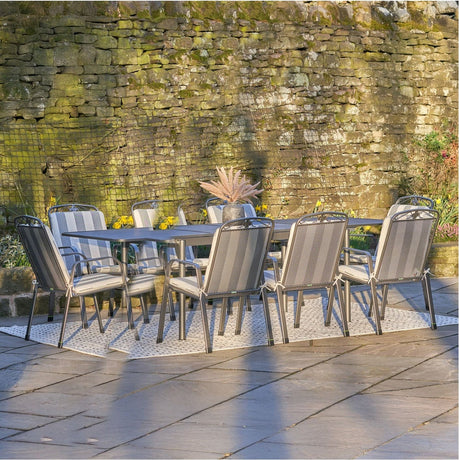 Savoy extendable rectangular dining set with eight grey rattan-style chairs and cushioned seats around a matching table, shown on a patio against a stone wall.