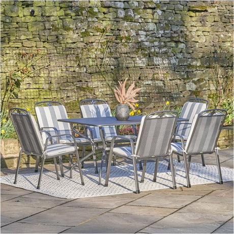 Savoy rectangular 6 seater dining set in grey with rattan-effect chairs and grey-white striped cushions, set on a garden patio against a stone wall.