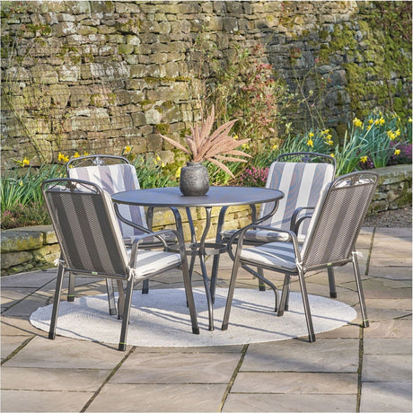 Savoy 4 Seater Dining Set with Cushions, 57cm round table and four grey stacking chairs with striped cushions, set on a stone patio near a mossy wall.