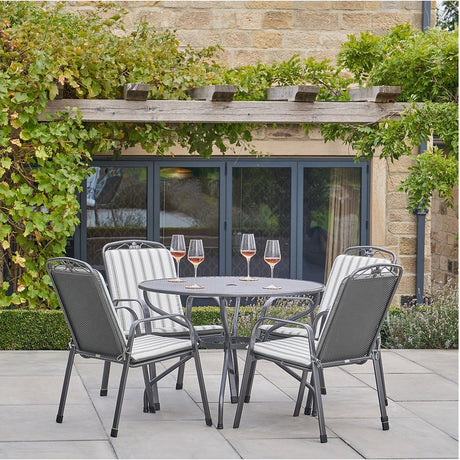 Savoy Round 4 Seater Dining Set with grey metal frame, round table and four chairs featuring grey striped cushions, shown on a patio beside a stone building.