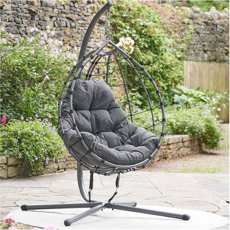 Lyon Anthracite Outdoor Single Hanging Chair with teardrop-shaped steel frame, curved stand, and dark grey cushioned seat, shown on a garden patio.