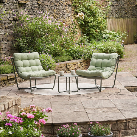 Clermont Moss Green Outdoor Lounging Set with two low-slung tufted lounge chairs and a round side table, steel frames, set on a patio in a garden setting.