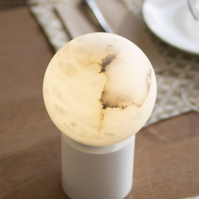 Halvessa LED rechargeable outdoor table lamp with a round alabaster globe showing grey veining, set on a slim white cylindrical base on a wooden table.