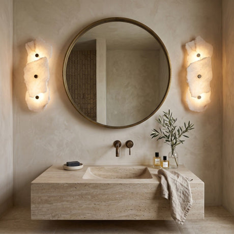 Frammenta LED 3 Light Fragment Alabaster Wall Light in Brass, mounted either side of a round mirror above a travertine washstand in a bathroom setting.