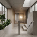 A minimalist interior with concrete and wood accents, large windows, indoor plants, a modern metal-railed staircase, and the Cosmos LED Large Pendant Light hanging in the hallway. The space feels open and well-lit.