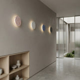 A minimalist hallway features four Pin LED Wall Lights in different colors, a light wood shelf with ceramic vases, and floor-to-ceiling glass doors that flood the space with natural light.