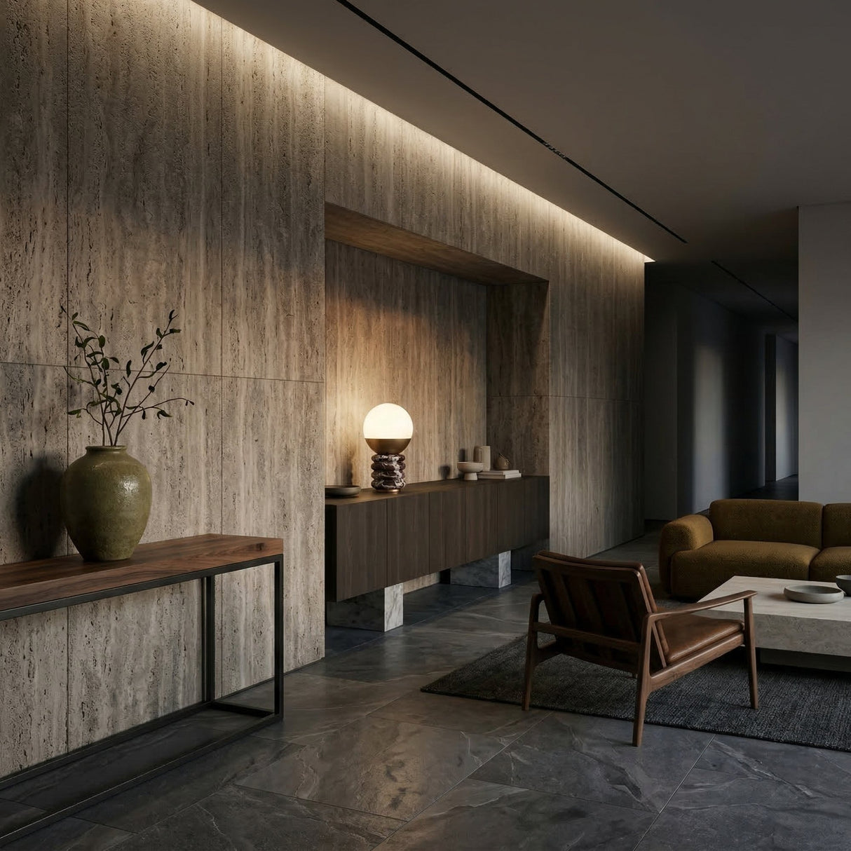 A modern living room with stone walls and floors featuring a wooden console table with a green vase, a brown armchair, a green sofa on a gray rug, and the Velar 1 Light Sculpted Marble Table Lamp in Brass & Purple Red on the sideboard.