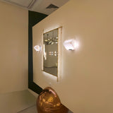Solviera LED alabaster rectangular wall mirror with brass inlay edging, mounted on a wall between two alabaster sconces in a softly lit hallway setting.