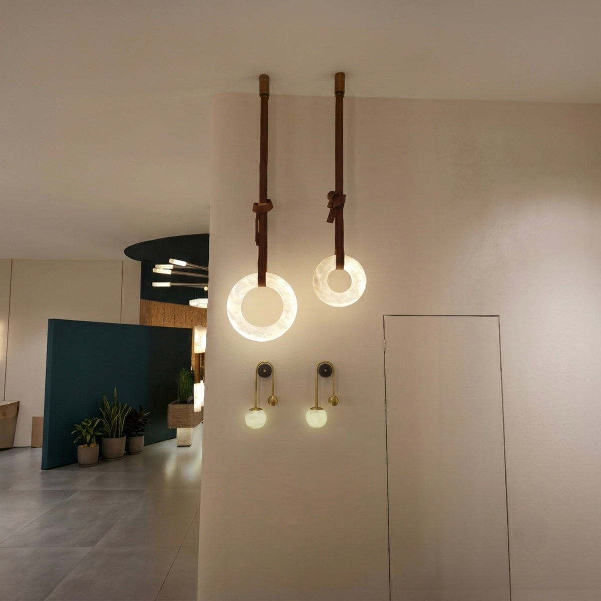 Cintura LED Alabaster Ring Chandelier pair hung on brown leather straps with copper fittings, illuminated warm-white in a modern hallway setting.
