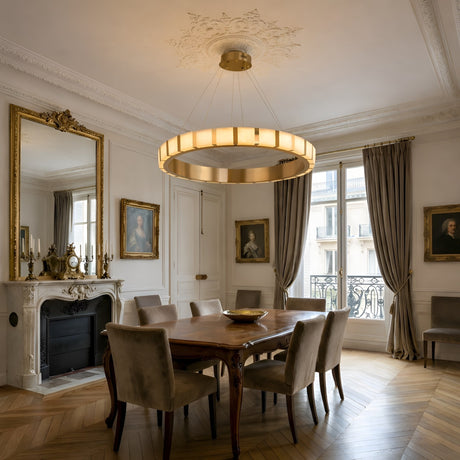 Elegant dining room with a large wooden table, gray upholstered chairs, ornate fireplace, gold-framed mirrors, classic paintings, tall windows with drapes, and the Strata LED Small Alabaster Chandelier – Soft White & Copper on a detailed ceiling.