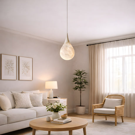 A bright, airy living room features a white sofa, round wooden coffee table with flowers, wicker chair, potted plant, framed wall art, large window with sheer curtains, and the Virello 1 Light Small Raindrop Alabaster Single Pendant Light in Soft White.