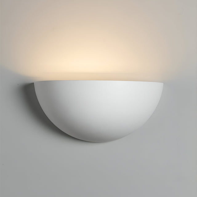 The Uplighter Plaster Wall Light features a modern, semi-circular design crafted from gypsum plaster. It casts soft, ambient light upwards against a plain white wall, with its minimalist aesthetic creating a warm and inviting atmosphere in any space.