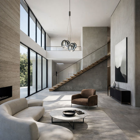A modern, minimalist living room with large windows, neutral-toned furniture, a curved sofa, circular coffee table, brown armchair, floating wooden staircase, abstract wall art, and the Diverso LED Pendant Light - Chrome as a contemporary lighting fixture.