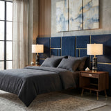 Modern bedroom with a blue upholstered headboard, abstract wall art, gray bedding, and wooden nightstands. Lunvera 1 Light Accent Ring Marble Table Lamp - Brass & Black adds elegance. Large window with sheer curtains brings natural light.