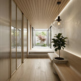 Minimalist hallway with light wood floors and ceiling, a built-in wooden bench, potted plant, and Verge 1 Light Pendant with smoked shade, plus smoked glass doors on one side and a view of a small courtyard garden with a tree.