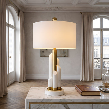 The Solaryn 1 Light Offset Alabaster Table Lamp in Brass & Soft White sits on a marble console table in an elegant room featuring tall windows, beige curtains, and parquet wood floors.