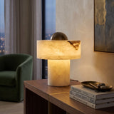 Cupolino Dome Alabaster Table Lamp in white with brass dome top, glowing on a console table beside books in a living room setting.