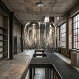 An industrial loft with exposed brick walls and large windows features the Symphonia 10 Light Metal Chain Veil Small Chandelier in nickel, its sleek ribbons hanging over a metal walkway for a dramatic modern touch.