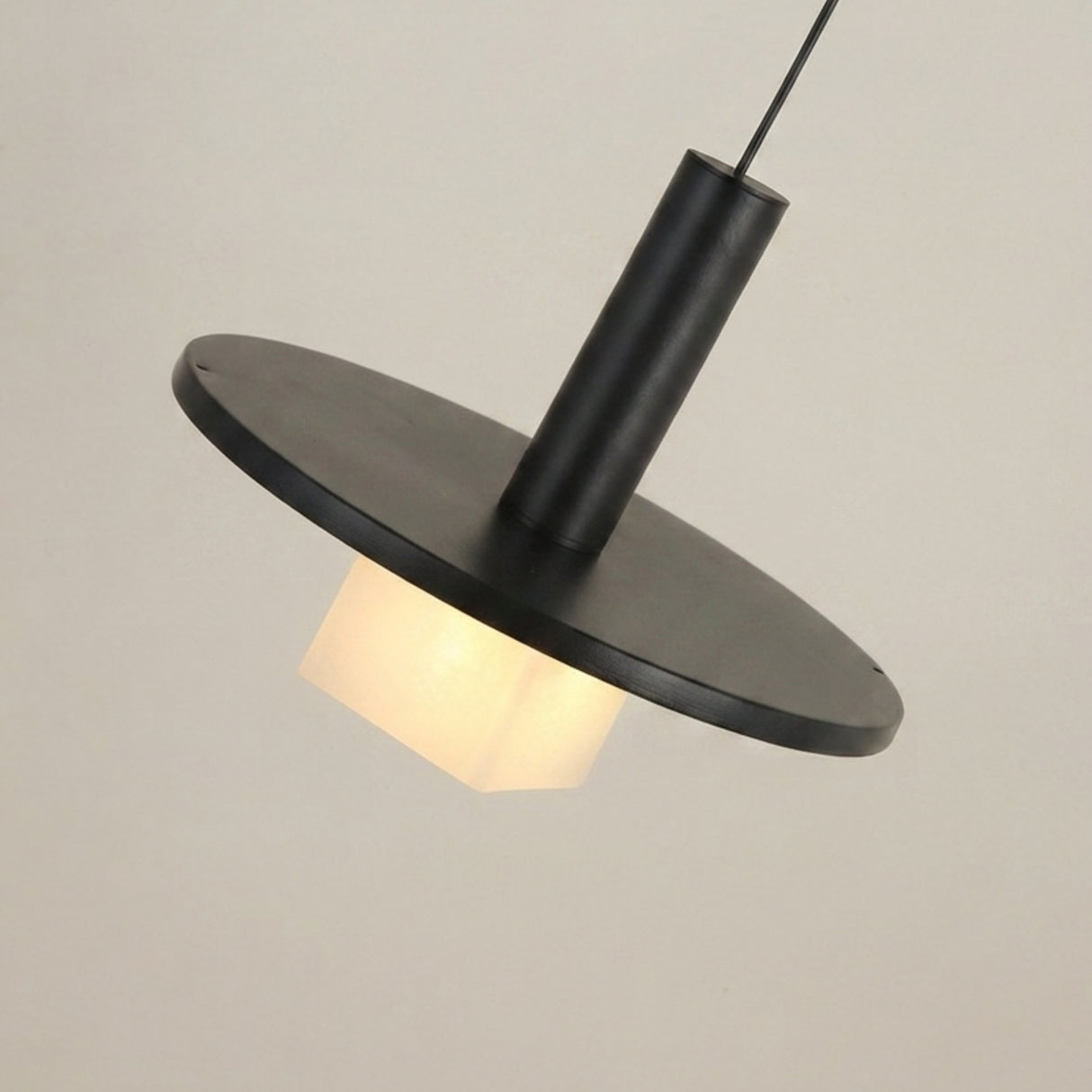 Norevia Cube Alabaster Pendant Light in matte black, with a wide disc canopy, slim cylindrical stem, and glowing alabaster cube shade, shown against a plain light background.