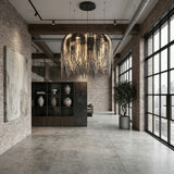 A modern loft with brick walls, large windows, concrete floor, an open shelving unit with vases, abstract painting, potted tree, and the Symphonia 10 Light Metal Chain Veil Small Chandelier in Nickel.