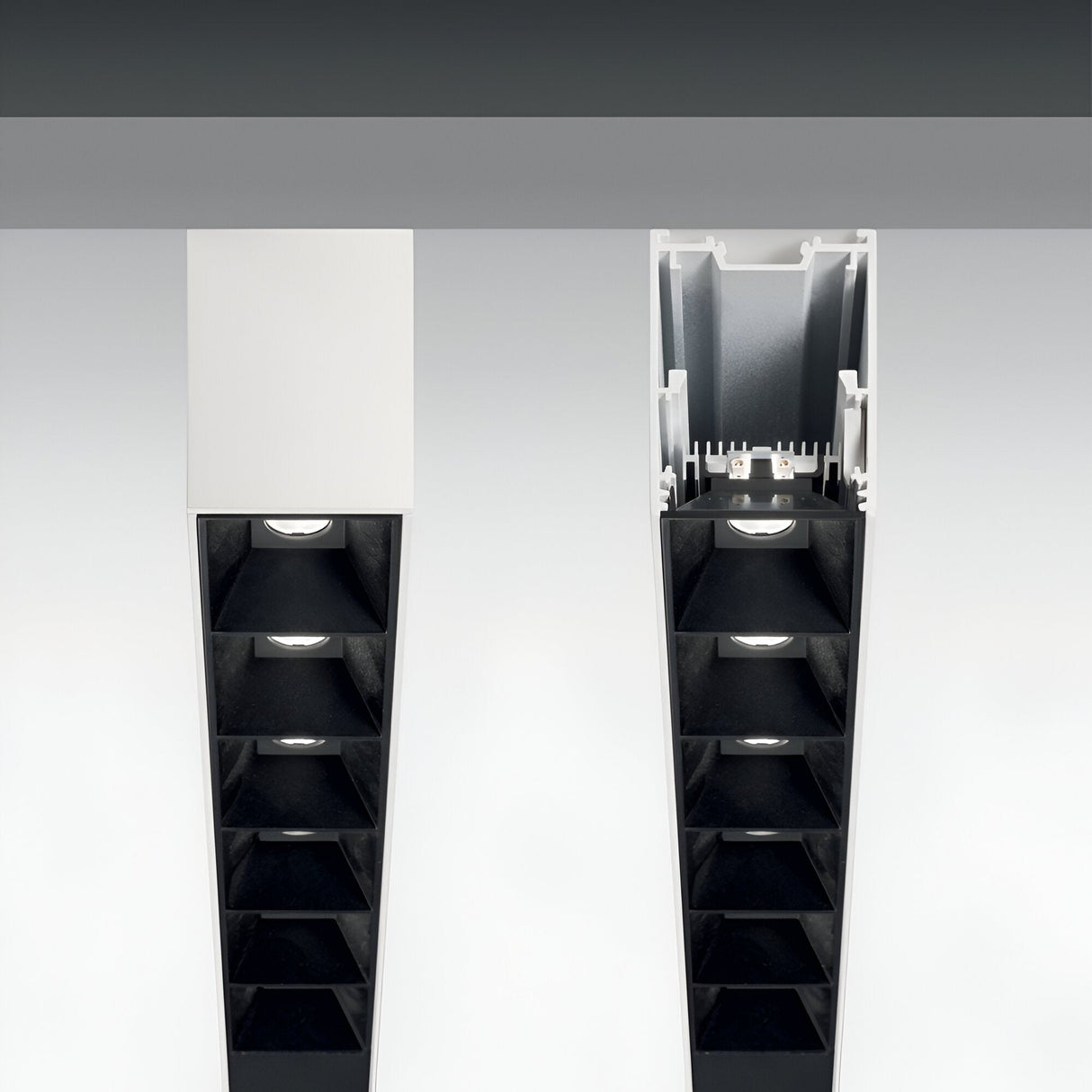 Close-up of two linear ceiling light fixtures with a modern design. The left fixture is the Sparx Linear LED Suspension Light, featuring a 30W output and 3000K color temperature, elegantly covered with a white panel and measuring 1805mm. Meanwhile, the right fixture is open, revealing multiple small light sources inside a rectangular black housing—a perfect example of energy-efficient lighting solutions.