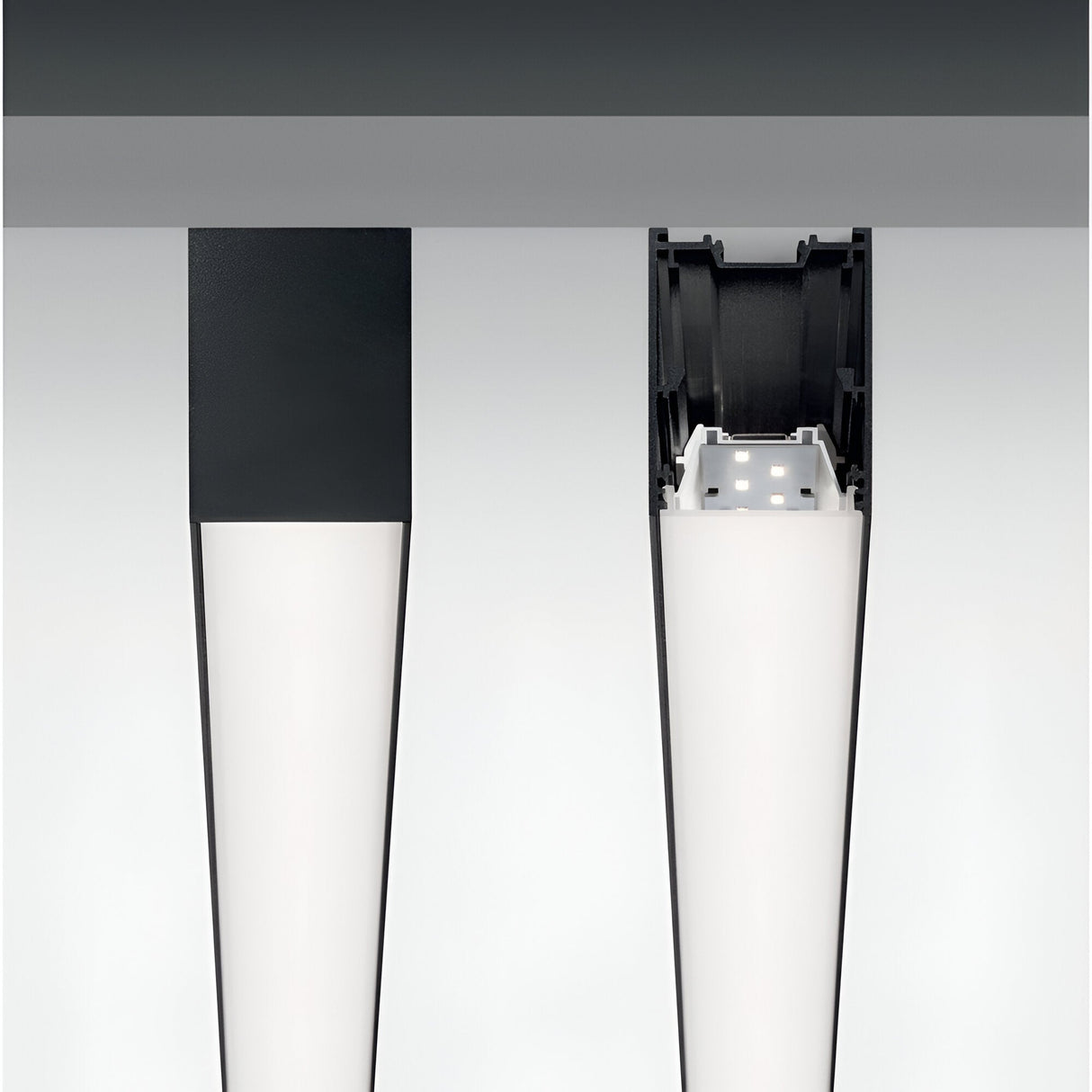 Close-up view of two ceiling-mounted rectangular Sparx Linear LED Suspension Lights, 27W 3000K - Black, measuring 1805mm. The left fixture is fully enclosed, while the right one reveals its interior components and wiring, providing a cross-sectional view. This sleek, modern design exemplifies energy-efficient illumination in a linear lighting system.